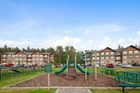 Apartment complex with a children's playground in front, surrounded by lush greenery and blue skies.