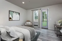 Modern bedroom with elegant decor, featuring a cozy bed, abstract art, and a scenic garden view through a glass door.