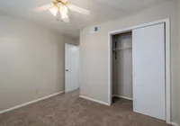Charming bedroom with soft beige walls, plush carpet, and a cozy closet, featuring a ceiling fan for comfort.