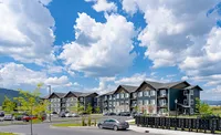 Modern apartment complex on a sunny day with a vibrant landscape, ample parking, and picturesque blue skies with fluffy clouds.