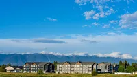 Charming apartment complex with stunning mountain backdrop under a vibrant blue sky.
