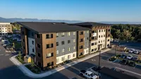 Modern apartment complex surrounded by lush greenery and scenic mountain views, offering ample parking and stylish exterior design.