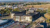 Scenic aerial view of modern apartment complex surrounded by lush greenery and rolling hills, offering ample parking and urban convenience.
