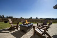 Inviting outdoor patio with Adirondack chairs surrounding a modern fire pit, offering scenic views of an open field and blue sky.