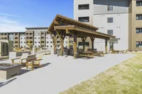 Modern apartment complex featuring a spacious outdoor area with wooden pergola, picnic tables, and cozy seating for community gatherings.