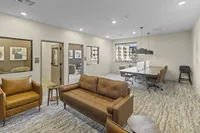 Modern office space featuring cozy leather seating, a conference table with stylish chairs, and large windows providing ample natural light.