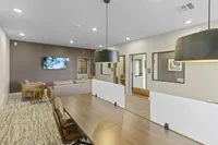 Modern coworking space with stylish furniture, featuring leather chairs, a large wooden table with dividers, and a cozy lounge area with a wall-mounted TV.