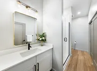 Sleek and modern bathroom featuring a spacious vanity with elegant lighting, chic mirror, and a glass-enclosed shower. Bright and airy with wood-look flooring and stylish decor touches.