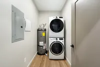 Modern laundry room with stacked washer and dryer, sleek water heater, and elegant wooden flooring.