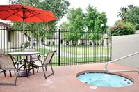 Charming outdoor patio at Camelot in Yuma with cozy seating, vibrant red umbrella, and inviting hot tub, overlooking lush green garden.