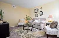 Inviting living room with plush seating, stylish decor, and a glass coffee table, accentuated by charming wall clocks and lush plants at Camelot Apartments in Arizona.