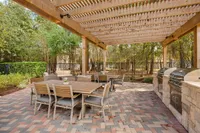 Charming outdoor patio at Raveneaux Apartments with elegant seating, shaded by a wooden pergola and equipped with modern barbecue grills, perfect for entertaining in a serene natural setting.