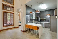 Chic modern community kitchen with sleek countertops, stylish pendant lighting, and a cozy breakfast bar with elegant orange seating at Raveneaux Apartments.