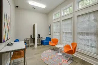 Raveneaux Apartments' contemporary lounge area featuring vibrant orange chairs, a sleek work station, and ample natural light from large windows.
