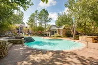 Beautiful apartment complex with a sparkling outdoor pool surrounded by lush greenery and stylish lounge seating, offering a serene resort-like ambiance at Raveneaux Apartments.