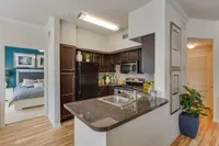 Modern apartment kitchen with sleek dark cabinetry, granite countertops, and stylish stainless steel appliances adjacent to a cozy, inviting bedroom at Raveneaux Apartments in Houston, TX..