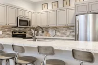 Clearview Apartments Clubhouse Modern kitchen in the clubhouse of Clearview Apartments with sleek gray cabinetry, stainless steel appliances, and stylish mosaic backsplash, featuring a spacious countertop with unique barstool seating.