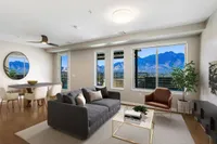 Sugarmont Living Room Townhome Staged View of Sugarmont Two Bedroom Townhome Showing Grey Couch with Grey Rug, Long Dining Table with White Chairs, Large Circular Mirror and Large Windows with Mountain Views