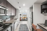 Modern apartment at Cottonwood Westside with sleek galley kitchen, stainless steel appliances, granite countertops, and an open living area with vibrant natural light.