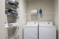 Modern laundry room at Cottonwood Westside with stacked towels and convenient shelving, featuring a washer and dryer in sleek white.