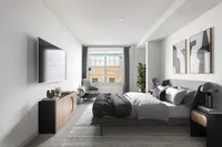 Modern, sunlit bedroom at Cottonwood Westside Apartments featuring a sleek, gray upholstered bed, stylish decor, large flat-screen TV, and a comfortable reading chair by the window.