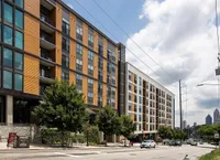 View of Cottonwood Westside, a contemporary apartment building exterior with striking orange accents, large windows, and lush greenery in an urban setting.
