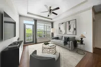 Living Room with Tray Ceiling Elegant living room at Heights at Meridian Apartments with stylish decor, featuring a plush gray sofa, modern armchair, and large windows inviting natural light, complemented by framed artwork and a chic ceiling fan.