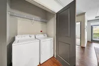 Washer & Dryer in Select Homes Modern apartment at Heights at Meridian with in-unit laundry featuring a sleek washer and dryer, complemented by stylish wooden flooring and a spacious hallway.
