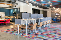 Find the perfect blend of work and collaboration in this vibrant community workspace. Vibrant coworking space featuring a stylish kitchen area with blue cabinets and red chairs, alongside a colorful, modern office setup with adjustable desks and comfortable seating at The Melrose Apts in Berry Hill.