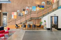 Enjoy the unique charm of this chic space at Apt CoWork at The Melrose. Modern coworking space with stylish brick walls, vibrant artwork, and a spacious seating area under a sleek staircase, perfect for creative gatherings at The Melrose Apartments in Tennessee.