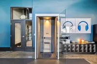 Our privacy pods are perfect spot to take meetings and will help you stay productive at Apt CoWork at The Melrose Modern office space featuring a sleek blue accent wall, a stylish phone booth, and eye-catching headphone artwork at The Melrose Apartments in Berry Hill, TN.