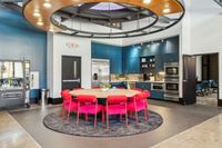 The Melrose Communal Kitchen Modern communal kitchen with vibrant red chairs around a circular table, surrounded by blue cabinets and equipped with stainless steel appliances, perfect for social gatherings at The Melrose in Nashville.