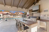 Elegant outdoor kitchen adjacent to a sparkling pool, featuring modern appliances and stylish seating for a luxurious lifestyle at Pavilions Apartments.