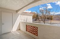 Charming apartment balcony at Pavilions Apartments with stucco walls, offering a sunny view of the neighborhood and clear skies.