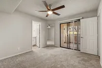 Bright bedroom with plush carpet, ceiling fan, mirrored closet doors, and a sliding glass door opening to a sunny balcony at Pavilions Apartments.