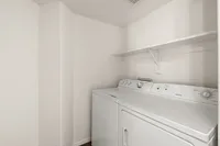 Modern laundry room at Pavilions Apartments with washer and dryer, featuring ample shelving and a crisp, clean design.
