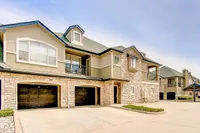 Charming two-story apartment exterior with stone facade, two-car garage, and cozy balcony in a serene neighborhood of Stonebriar of Frisco Apartments.