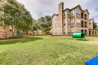 Charming apartment complex, Stonebriar of Frisco Apartments, featuring elegant architecture with lush green lawns and a cozy play area for relaxation.