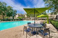 Luxe apartment community showcasing a pristine outdoor pool with elegant umbrellas and comfortable lounge chairs, surrounded by lush greenery at Stonebriar of Frisco Apartments.