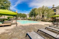 Inviting outdoor pool area at Stonebriar of Frisco Apartments with elegant lounge chairs and vibrant green canopies, nestled amidst lush greenery and modern apartment buildings.