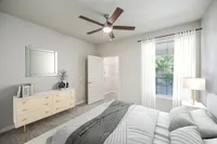 Bright and inviting bedroom at Stonebriar of Frisco Apartments with modern decor featuring a stylish dresser, ceiling fan, and large window with sheer curtains.