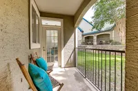 Charming apartment patio at Stonebriar of Frisco with cozy seating, offering a serene view of lush green garden and elegant stone architecture.