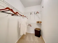 Spacious walk-in closet at Stonebriar of Frisco Apartments with sleek white walls, modern wire shelving, and stylish wooden hangers for a luxurious living experience.