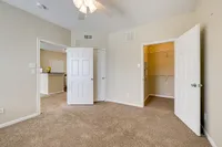 Inviting bedroom at Stonebriar of Frisco Apartments with plush carpet, open closet space, and a glimpse of a modern kitchen. Bright and spacious living.