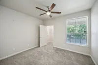 Bright bedroom with modern ceiling fan, plush carpet, and large window offering green views at Stonebriar of Frisco Apartments.