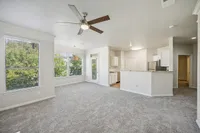 Bright and airy living space with plush carpeting, ceiling fan, large windows, and an open kitchen with modern cabinetry at Stonebriar of Frisco Apartments.