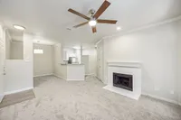 Chic living room at Stonebriar of Frisco Apartments with plush carpeting, elegant ceiling fan, and cozy fireplace, adjacent to a modern kitchen with granite countertops.