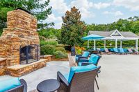 Charming outdoor patio featuring a stone fireplace, cozy wicker furniture with blue cushions, and a shaded pergola, perfect for relaxation and entertaining at Summer Park Apartments.
