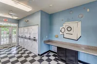 Bright and modern laundry room at Summer Park Apartments with vibrant blue walls, playful washer art, black and white checkered floor, and convenient counter space.