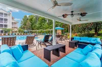 Summer Park's luxurious poolside area featuring a covered lounge with plush blue seating, surrounded by lush greenery and modern amenities.